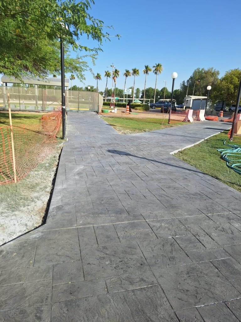 Newly paved walkway featuring stamped concrete, surrounded by lush greenery and palm trees, with construction barriers in the background  Ideal for enhancing outdoor spaces in residential or commercial areas 