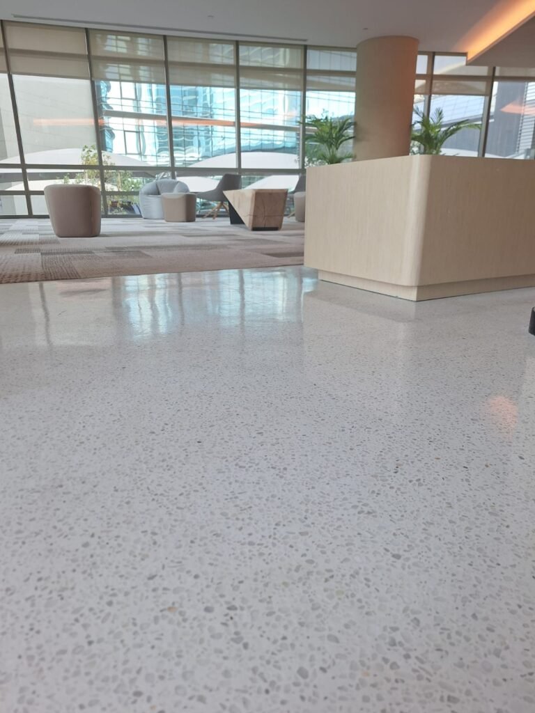 Modern interior space featuring polished terrazzo flooring, large windows allowing natural light, and contemporary furniture arrangements  The design emphasizes a clean and inviting atmosphere, ideal for relaxation and social interaction 