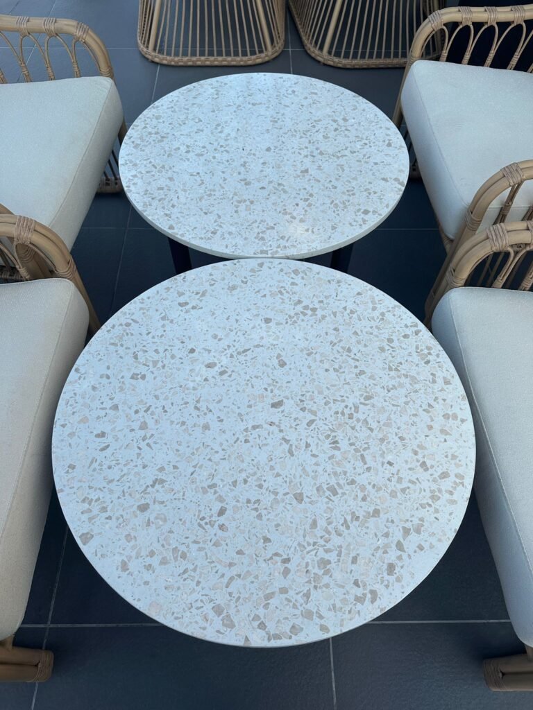 Two round terrazzo coffee tables positioned between modern rattan chairs on a sleek tiled floor, creating a stylish and inviting outdoor seating area 
