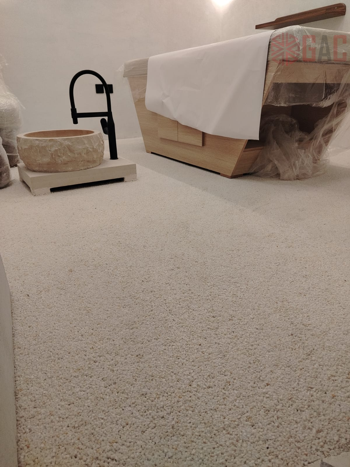 Modern bathroom interior featuring a stone sink with a black faucet, a wooden bathtub covered in protective plastic, and a textured carpeted floor 
