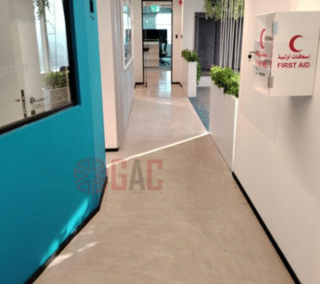 Interior view of a modern office hallway featuring blue walls, a first aid station, and greenery along the walls, designed for a professional environment 
