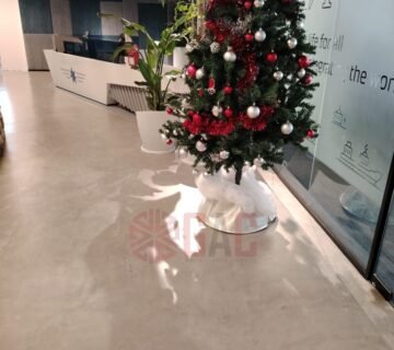 Christmas tree decorated with red and white ornaments in a modern office space, featuring a concrete floor and a glass wall with company branding 