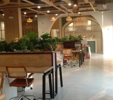 Modern office interior featuring wooden desks, ergonomic chairs, and abundant greenery, creating a vibrant and inviting workspace  Natural light floods the area, enhancing the contemporary design and fostering a productive atmosphere 