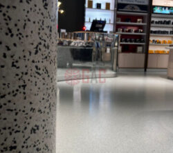 Interior view of a retail space featuring a polished floor, a speckled column, and a modern checkout counter with merchandise displays in the background.